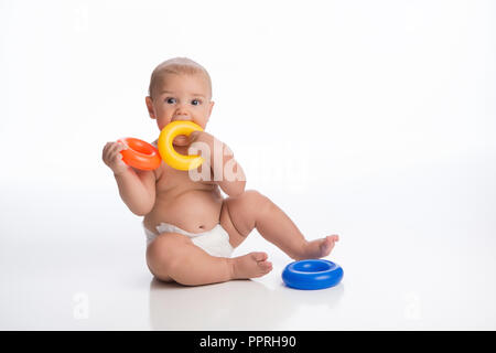 Ein sieben Monate altes Baby Boy, mit einem niedlichen Ausdruck, indem ein Spielzeug Ring in seinem Mund. Im Studio auf einem weißen, nahtlose Kulisse erschossen. Stockfoto