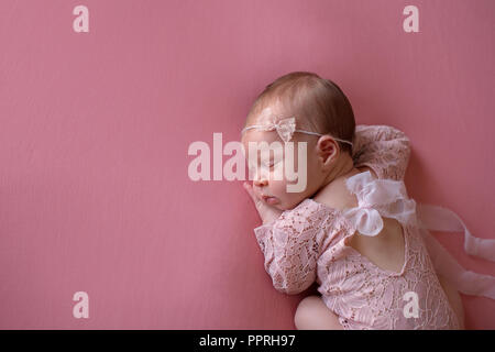 Eine schöne, Schlafen, neugeborene Mädchen mit einem rosa, Spitze Romper und Spitze Bügel. Im Studio mit einem rosa Hintergrund. Stockfoto