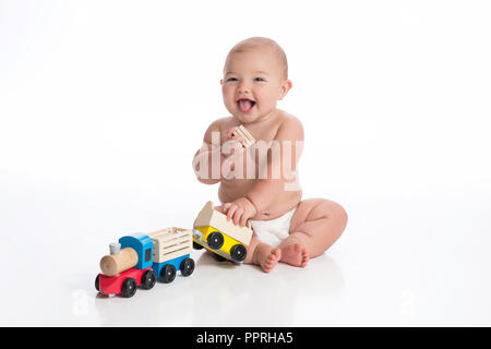 Ein lächelndes sieben Monate alten Baby Junge spielt mit einem hölzernen Zug. Im Studio auf einem weißen, nahtlose Kulisse erschossen. Stockfoto