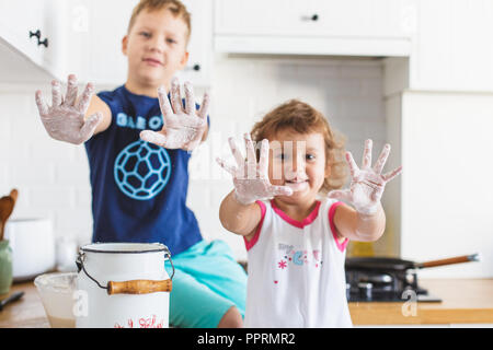 Bruder und Schwester Vorbereitung Teig für Pfannkuchen in der Küche. Konzept der Lebensmittelzubereitung, weiße Küche für den Hintergrund. Casual Lifestyle Foto serie Stockfoto