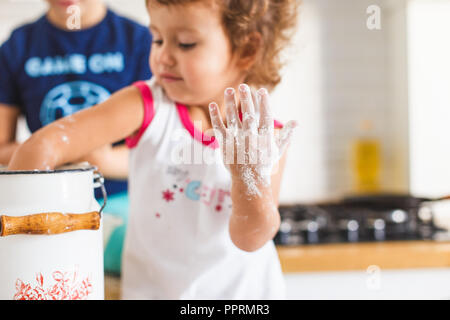 Bruder und Schwester Vorbereitung Teig für Pfannkuchen in der Küche. Konzept der Lebensmittelzubereitung, weiße Küche für den Hintergrund. Casual Lifestyle Foto serie Stockfoto