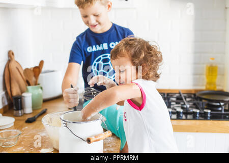 Bruder und Schwester Vorbereitung Teig für Pfannkuchen in der Küche. Konzept der Lebensmittelzubereitung, weiße Küche für den Hintergrund. Casual Lifestyle Foto serie Stockfoto