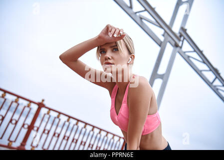 Nach dem Joggen müde. Schöne junge Frau im Sport Kleidung Biege- und müde, während auf der Brücke stehen und urbane Aussicht im Hintergrund Stockfoto