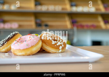 Ein paar leckere Donuts auf einem Tablett mit mehr auf Display hinter Stockfoto
