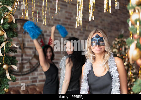 Frau mit eleganten schwarzen Kleid mit Maske viel Spaß bei der Party des Neuen Jahres. Tanzende Frauen auf Hintergrund Stockfoto