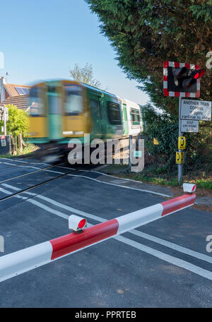 Eine schnelle Beschleunigung der Zug nähert sich einem automatischen Hälfte Barriere Bahnübergang von Network Rail betrieben. Stockfoto