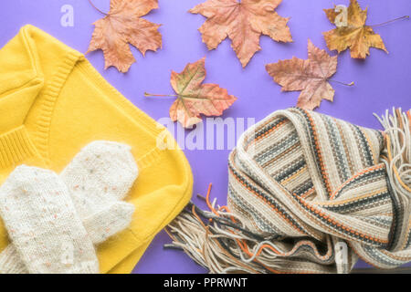 Herbst Winter Fashion saisonale Konzept pullover Strickjacke skandinavischen Strickschal und weißen flauschigen hausgemachte Handschuhe Fallen gefallen Ahornblätter auf Papier Stockfoto