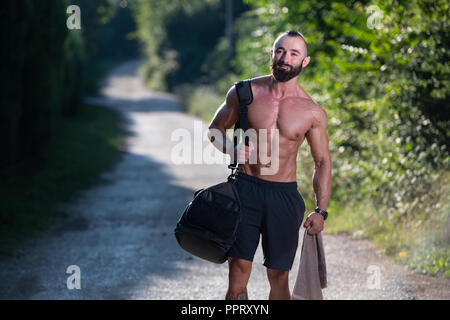 Bart Mann mit Sporttasche draußen im Park und geht ins Fitnesscenter in der Turnhalle Stockfoto