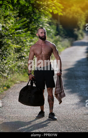 Bart Mann mit Sporttasche draußen im Park und geht ins Fitnesscenter in der Turnhalle Stockfoto