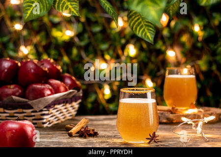 Lecker frischen Apfelwein Glas mit aromatischen Anis und Zimt liegen in der Nähe von Frische rote Äpfel auf Bauholz Tischplatte in Garten in Abend Stockfoto