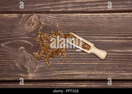 Viele von ganzen frischen braunen Leinsamen mit Holz- schaufel flatlay auf braunem Holz Stockfoto