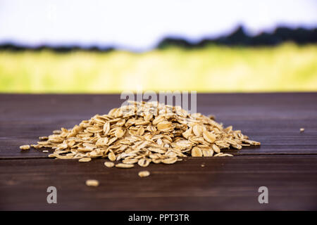 Menge ganze Wohnung rohe Haferflocken Heap mit grünen Weizenfeld im Hintergrund Stockfoto