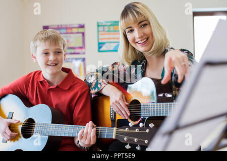Lehrer helfen männliche Kursteilnehmer zu spielen Gitarre im Musikunterricht Stockfoto