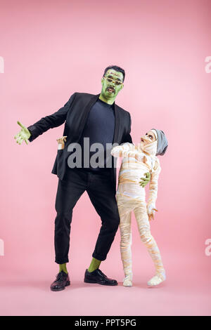 Halloween Familie. Gerne Vater und Kinder Mädchen in Halloween Kostüm und Make-up. Blutige Thema: Die verrückten maniak Gesichter auf Pink Studio Hintergrund Stockfoto