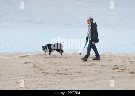 Ein Mann, der seinen Hund an der Küste auf den Fistral Beach in Newquay in Cornwall. Stockfoto