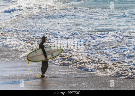 Ein surfer Holding sein Surfbrett stehend auf der Uferlinie auf den Fistral Beach in Newquay in Cornwall. Stockfoto