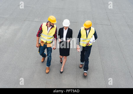 Ansicht der weiblichen Architekten und männliche Arbeitnehmer in Helmen mit Zwischenablage und Blueprints Stockfoto