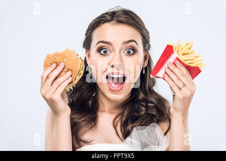 Close-up Portrait von schockiert junge Braut im Brautkleid mit Burger und Pommes frites an Kamera isoliert auf weißem suchen Stockfoto