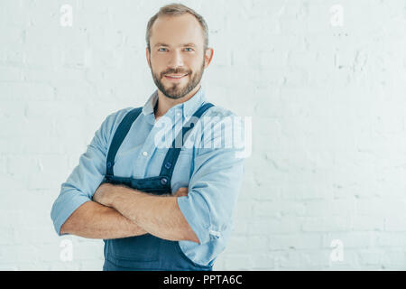 Lächelnd bärtigen Arbeiter in Overalls mit verschränkten Armen posing Stockfoto