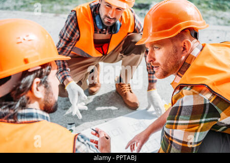 Nahaufnahme der Gruppe der Bauherren in harte Hüte in Gespräch über Blueprint Stockfoto