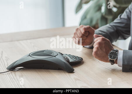 7/8 Schuß von Geschäftsmann vor Conference Phone sitzen und die fäuste im Büro Stockfoto