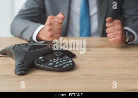 7/8 Schuß von Geschäftsmann vor Conference Phone sitzen und die fäuste im Büro Stockfoto