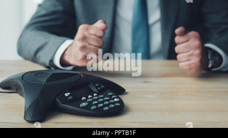 7/8 Schuß von Geschäftsmann vor Conference Phone sitzen und die fäuste im Büro Stockfoto