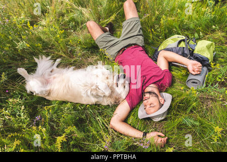 Blick von oben auf die Reisenden und Golden Retriever Hund liegend auf grünem Gras mit Rucksack Stockfoto