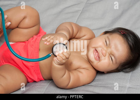 Happy Baby Mädchen spielen mit Stethoskop in der Arztpraxis bei entwicklungspolitischen Check-up Stockfoto