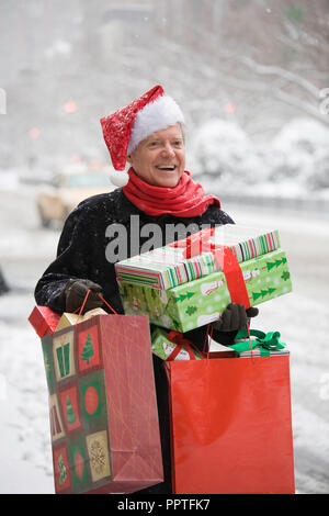 Freudige reifer Mann Lager Weihnachtsgeschenke an einem Verschneiten New York City Street, USA Stockfoto