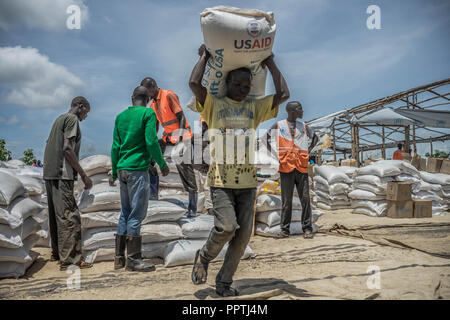 Uganda. 7. Mai, 2018. Eine sudanesische Flüchtlinge gesehen, die eine Packung mit 50 kg Maniokmehl oben auf dem Kopf. Die Bidi Bidi Flüchtling Siedlung im Norden Ugandas in der Nähe der sudanesischen Grenze ist derzeit das größte Flüchtlingslager der Welt, Hosting über 250.000 sudanesische Flüchtlinge im Süden des Konflikts. Das Welternährungsprogramm ist die Bereitstellung von monatlichen grundlegende Lebensmittel für die Flüchtlinge in der Siedlung. Credit: Alda Tsang/SOPA Images/ZUMA Draht/Alamy leben Nachrichten Stockfoto