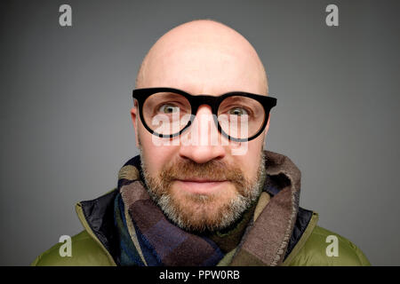 Fröhlicher Kerl lächelt glücklich. Zuversichtlich glatzköpfige Mann mit Brille warmer Schal. Stockfoto