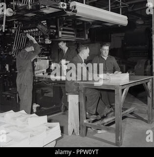 1950, historische, männliche Arbeitnehmer in Overalls in der Print Factory auf der Suche und Überprüfung in den Abschnitten einer Zeitschrift kommt eine große Presse, Stockfoto