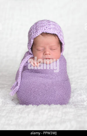 Zwei Wochen alte Neugeborene Mädchen mit einem Lavendel, gehäkelte Mütze. Sie schläft aufrecht, während sie sich in einer hell-lila Stretchfolie. Stockfoto