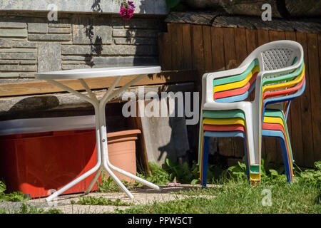 Die Sonne scheint auf freundlich Farbige gestapelt Kunststoff Gartenstühle und einen Tisch im Garten Stockfoto