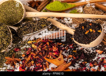 Von oben der Löffel aus Holz und Metall von unterschiedlichen Formen mit farbigen verschüttete Gewürze und Tees auf weissem Holztisch Stockfoto