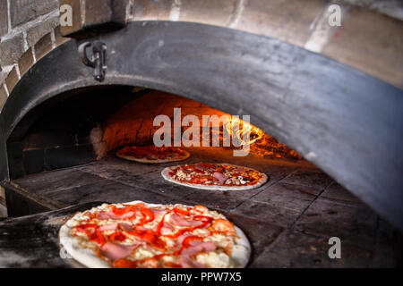 Pizza in den Ofen. Ein gutes Feuer brennt im Ofen. Pizza in den Ofen. Drei Pizzas im Ofen Stockfoto