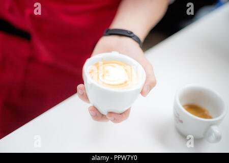 Barista hält eine Tasse mit einem figurativen Kaffee Latte in der Form eines Herzens Stockfoto
