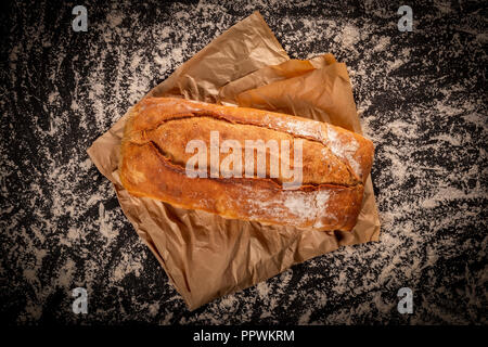 Von oben geschossen von Rustikalen hausgemachtes Brot Brot auf Pergament Papier oben auf Tabelle in weißes Mehl Stockfoto