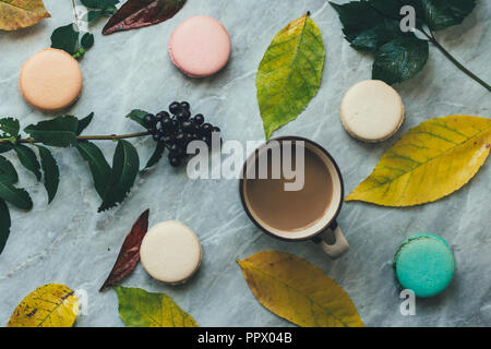 Herbst gelbe Blätter, eine Tasse Kaffee und Pastell Französische macarons Kuchen auf einem Marmor Oberfläche. Flach Zusammensetzung von oben, Ansicht von oben. Stockfoto