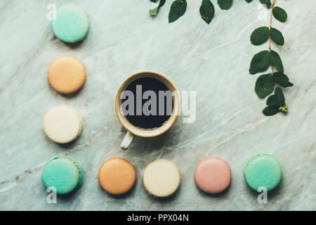 Blätter, eine Tasse Kaffee und Pastell Französische macarons Kuchen auf einem Marmor Oberfläche. Flach Zusammensetzung von oben, Ansicht von oben. Stockfoto
