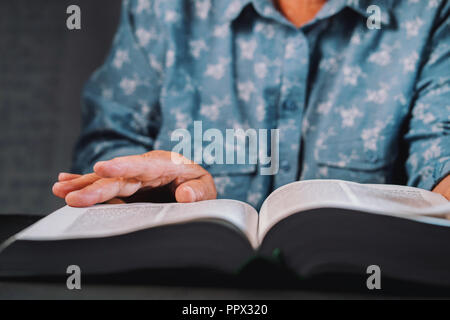 Alte Frau durch die Seiten des Buches spiegeln. Großmutter mit Bibel. Konzentriert Altersrentner mit Falten der Hände auf der Suche nach Informationen in der Bibliothek Stockfoto