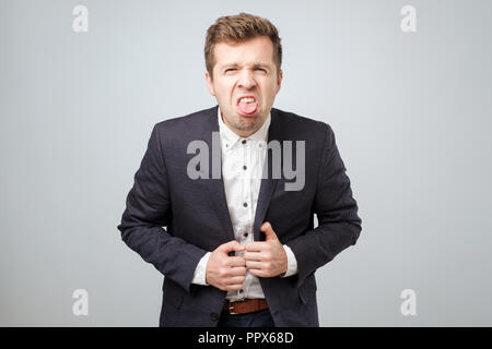 Ein junger Mann im Anzug mit einer Grimasse der Abscheu auf seinem Gesicht. Er setzt er seine Zunge heraus. Stockfoto
