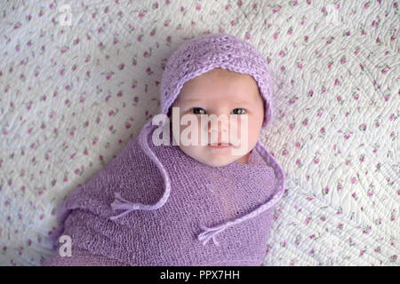 Einen Monat altes Baby Mädchen mit einem Motorhaube und Gepuckte in einem Lavendel Lila wickeln. Stockfoto