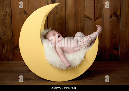 Studio Portrait von ein Gähnen, ein Monat altes Baby Mädchen liegt auf einem Mond geformt posing Prop. Stockfoto