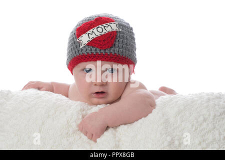 Ein 2 Monate altes Baby auf dem Bauch liegend auf einer weißen Decke. Er trägt ein gehäkelter Hut, der sagt, "Om". Im Studio gedreht auf einem weißen Ba Stockfoto