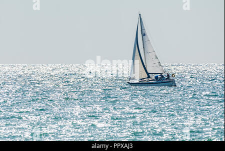 Einzelne person Yacht segeln auf See mit der Morgensonne funkelnden im Ozean, in Großbritannien. Stockfoto