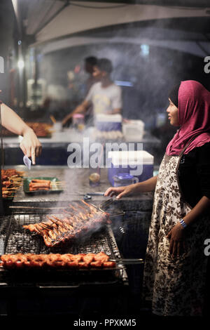 Muslimische Frau kocht gegrilltes Hühnchen am Nachtmarkt in Kota Kinabalu, Sabah, Borneo, Malaysia Stockfoto