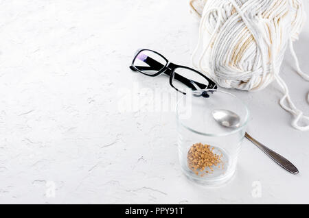 Glas mit Kaffee Korn, weiß stricken Threads und glasseson auf weißem Beton strukturierte Tabelle, selektiver Fokus, Kopieren, Ansicht von oben, Stockfoto