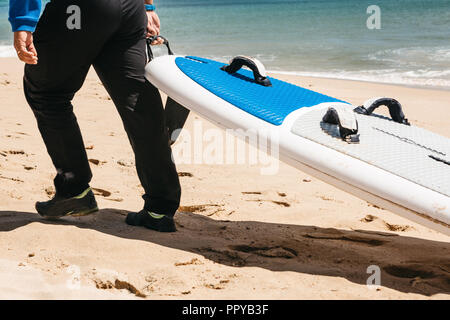 Person trägt ein Surfbrett am Strand. Stockfoto